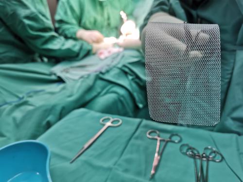 A surgeon prepping hernia mesh for an operation on a sterile table.