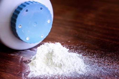 A container of Talcum Powder on its side spilling onto a hardwood floor.