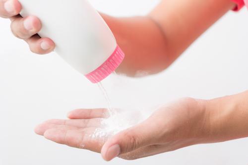 A closeup shot of a woman applying talcum powder to her hands from a white bottle.