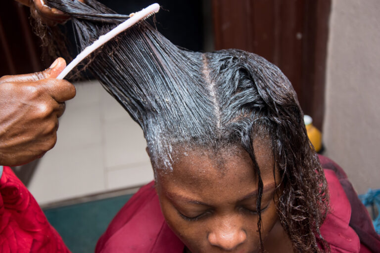 African American Black Woman getting hair relaxer or hair straightener treatment at the salon