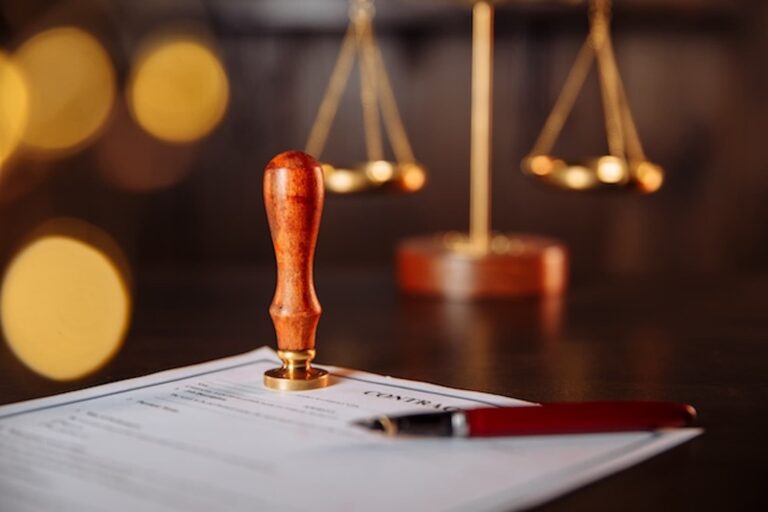 A lawyer's public pen and stamp on a contract with a scale in the background.