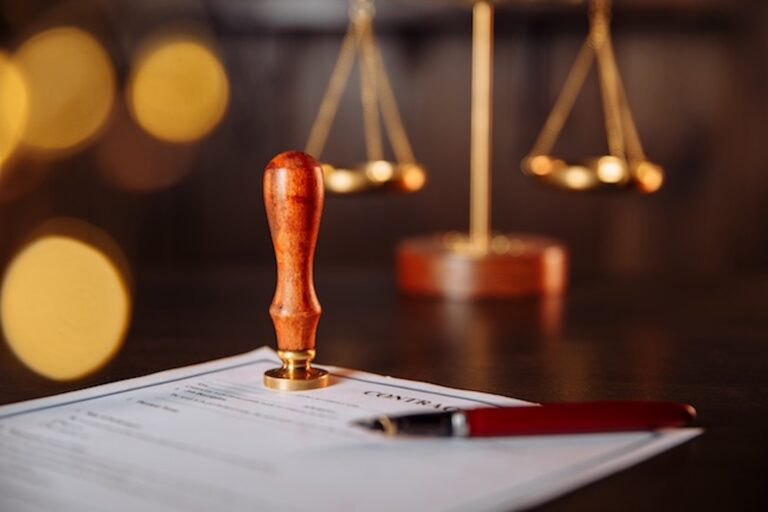 A lawyer's public pen and stamp on a contract with a scale in the background.