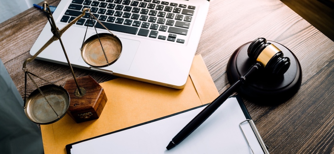 What Are Mass Tort Damages and Their Impact? A laptop, gavel, scale, clipboard, and manila envelope sitting on a brown wooden desk.