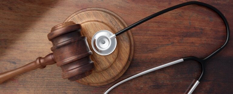 A gavel and a stethoscope on a brown wooden desk. This image is representing pharmaceutical negligence claims.