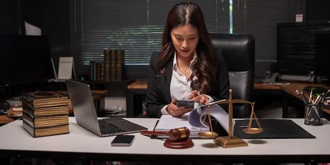 A female lawyer is working late at her desk, surrounded by law books and a gavel, as she prepares a multi-district litigation case for injured plaintiffs.
