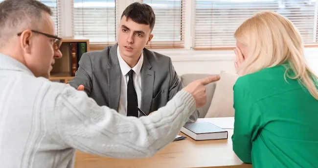 An attorney is mediating a discussion between an elderly couple during a product liability litigation consultation about defective medical device claims.