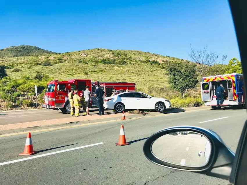 Emergency responders assisting at a car accident on a busy San Diego highway with traffic in the background.