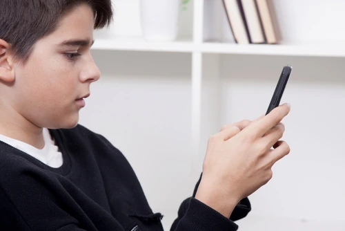 Boy at home with mobile phone representing Roblox grooming