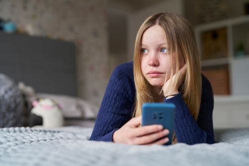 An image of a young girl holding her phone in her bedroom due to social media represents a social media addiction lawsuit case.