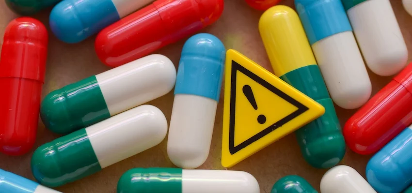What Is Failure to Warn and Why Does It Matter in Mass Tort Cases? A small yellow warning triangle with an exclamation point sits among scattered colorful medication capsules- highlighting the danger of failure to warn consumers about serious drug side effects and pharmaceutical risks within the USA.